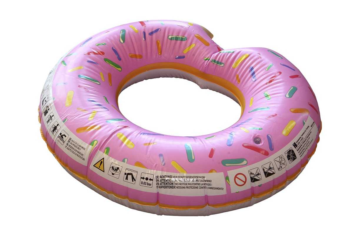 Rosa aufblasbarer Schwimmreifen in Donut-Form mit bunten Streuseln und angebissener Stelle. Unten weiße und orangefarbene Ränder wie Zuckerguss und Teig. Mehrsprachige Warnhinweise und Symbole sind aufgedruckt.